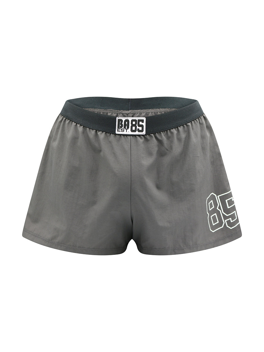 Grey athletic shorts with a black waistband and '85' branding on a white background