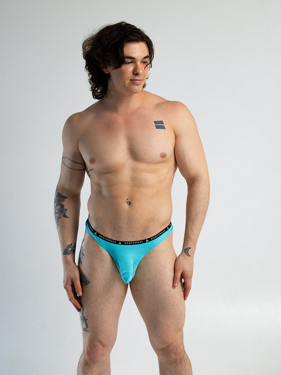 Front view of a man wearing a light blue thong with a sleeved pouch and Body Aware branded waistband.