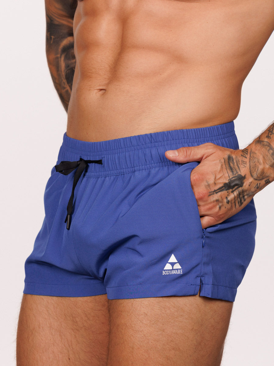 Closeup view of a male model wearing blue Body Aware square leg gym shorts 