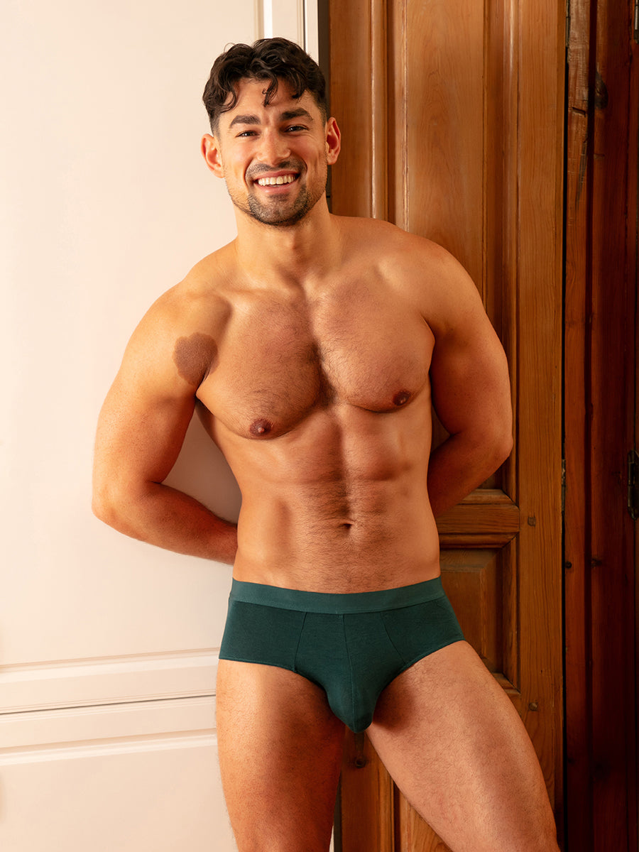 A man wearing teal green Body Aware briefs, standing in a doorway.