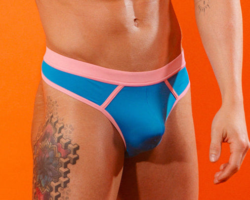 Front view of a man wearing a blue thong with pink trim against an orange background.