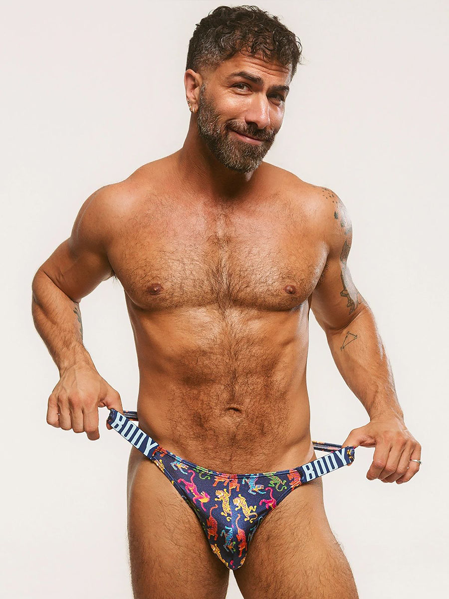 A man wearing a navy blue satin thong with a colorful tiger print and a Body Aware branded waistband.