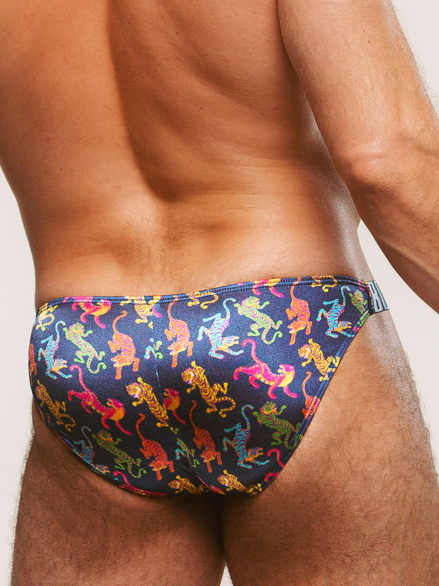 Back view of a man wearing navy blue satin briefs with a colorful tiger print, against a plain background.