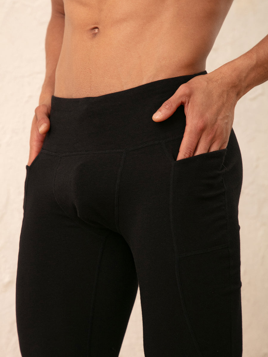 Close-up of a person wearing black high-waisted leggings with side pockets, shown from the waist to upper thighs against a light neutral background.