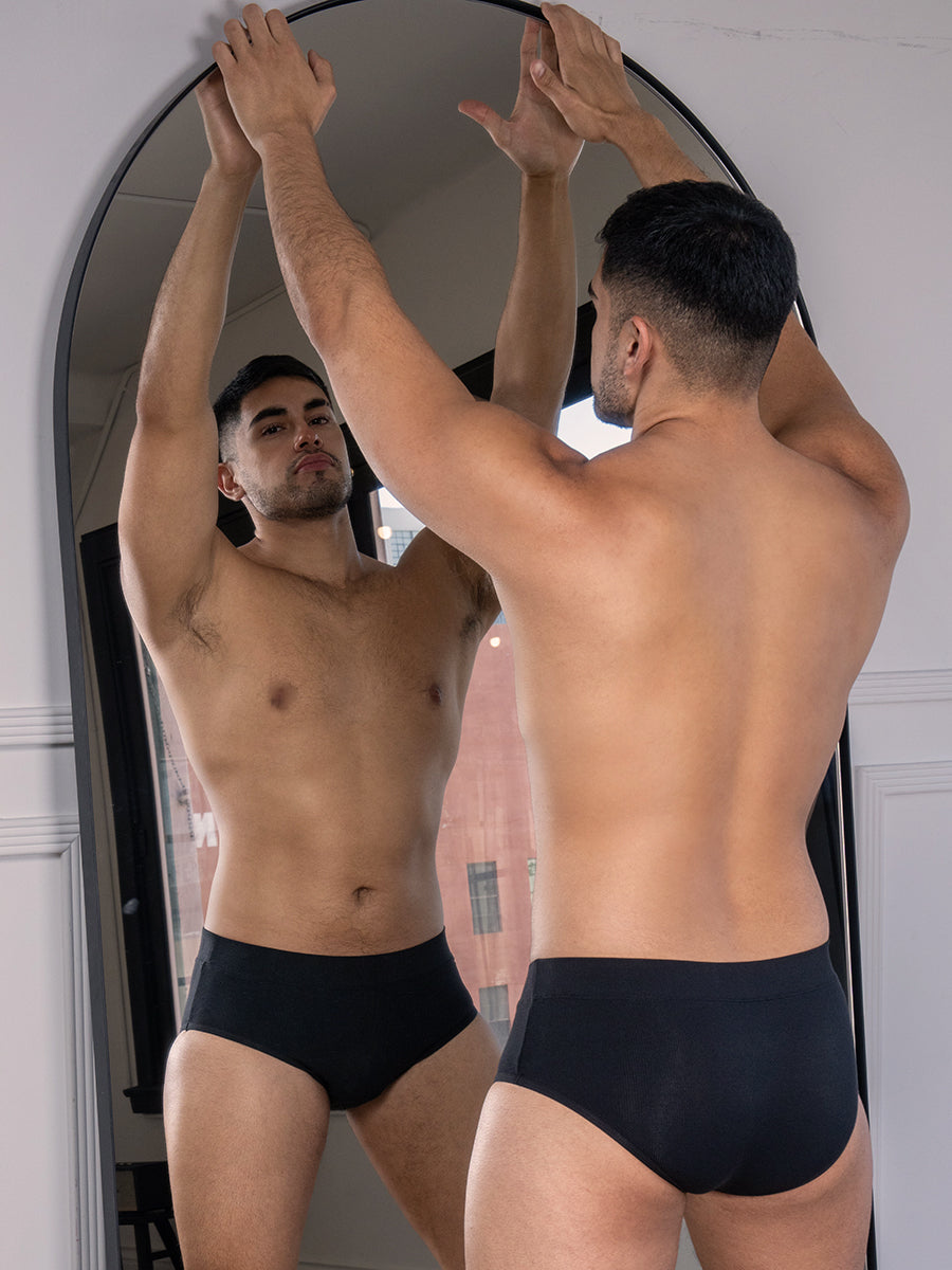 A man wearing black underwear briefs standing in front of a mirror.