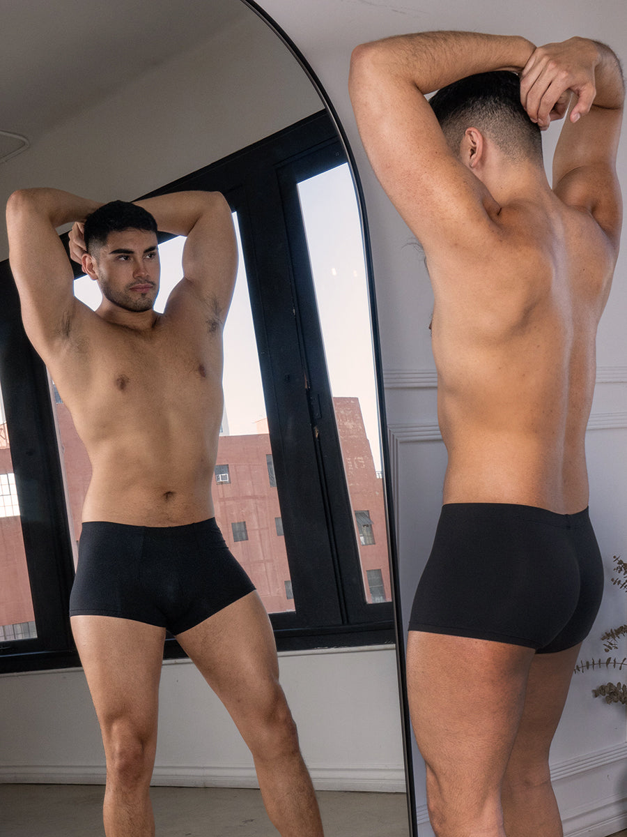 A man wearing black boxer briefs standing in front of a mirror.