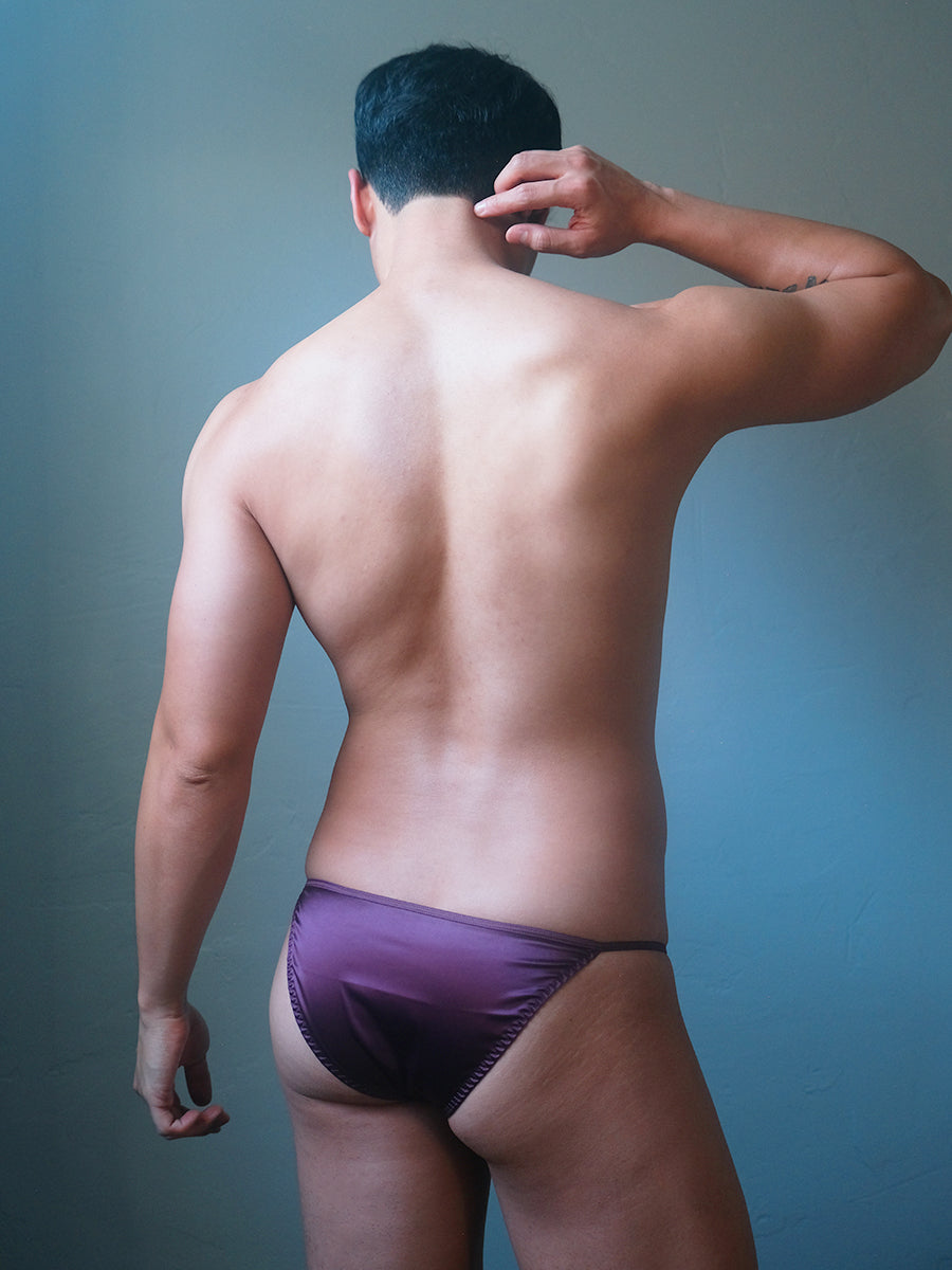 Back view of a male model wearing a Body Aware purple men's bikini brief