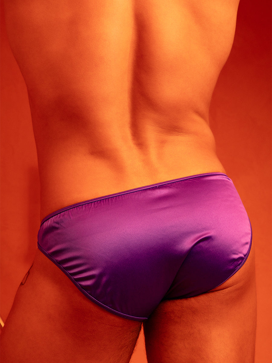 Closeup rear view of a man in purple satin underwear briefs, against an orange background.